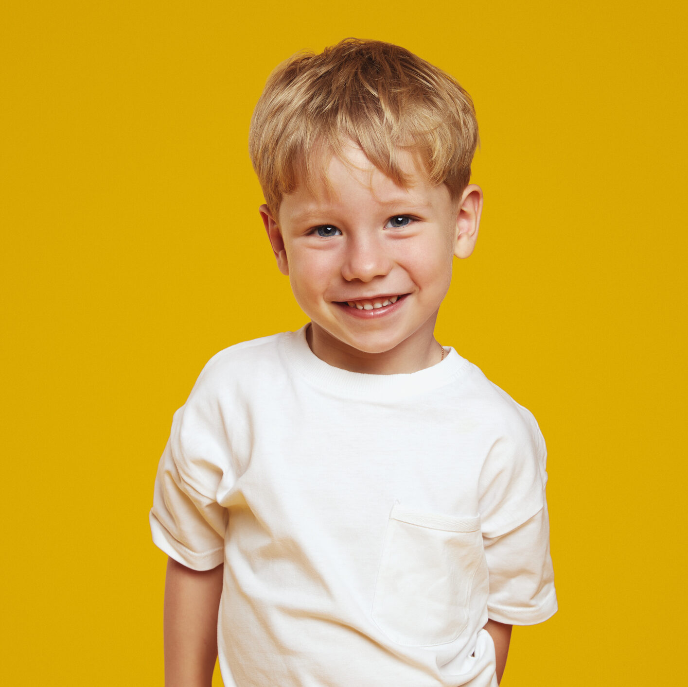 Happy Little Blonde Male Kid Boy In White Tshirt Laughing At Camera Against Orange Background